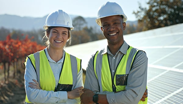 a woman and a man both wearing a yellow safety vest and helmets smiling at the camera