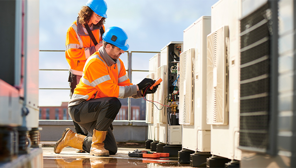 two battery storage technicians in long sleeved orange vests and blue hard hat assessing a battery storage unit