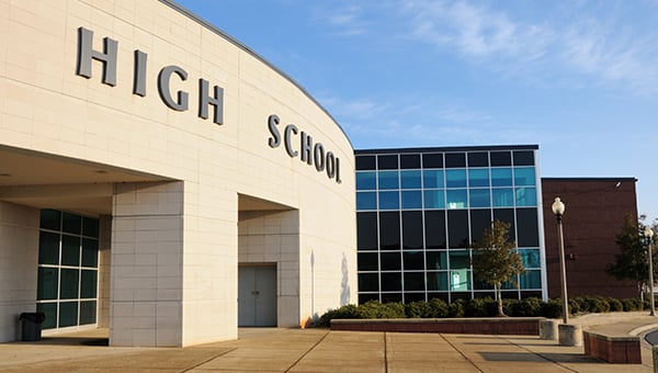 Exterior of a modern high school building with curved stone facade, large windows, and the words “High School” displayed on the front.