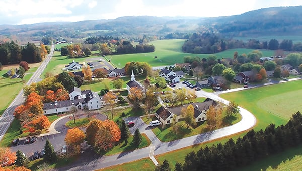 Aerial view of a small residential community with houses, roads, green fields, and trees in autumn colors.