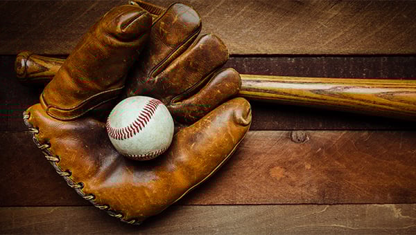 Baseball glove holding a baseball next to a wooden bat on a worn wooden surface.
