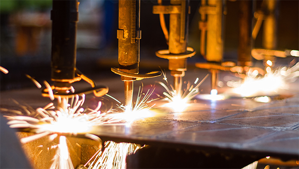 Industrial machines cut metal with bright sparks flying as multiple torches work along a sheet