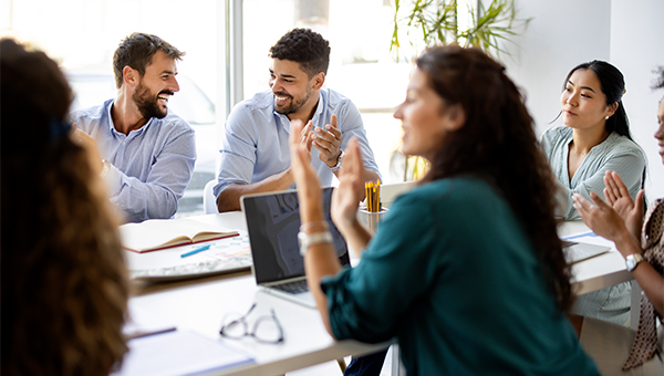 Small group sitting around a table, clapping during a meeting with notebooks and a laptop on the desk.