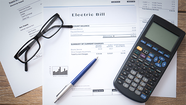 Electric bill statement on a desk with a calculator, pen, and eyeglasses, showing charges and account details.