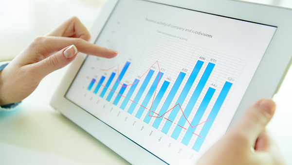 Close-up of hands interacting with a tablet displaying a bar chart and line graph of company performance data.