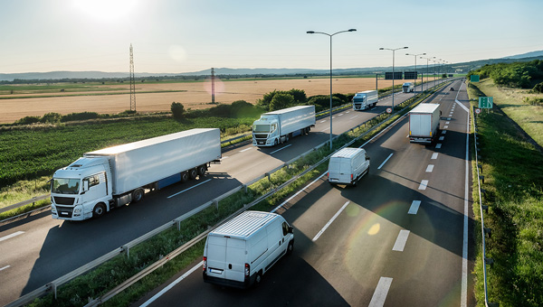 Multiple trucks and vans driving along a highway through a rural landscape under clear skies.