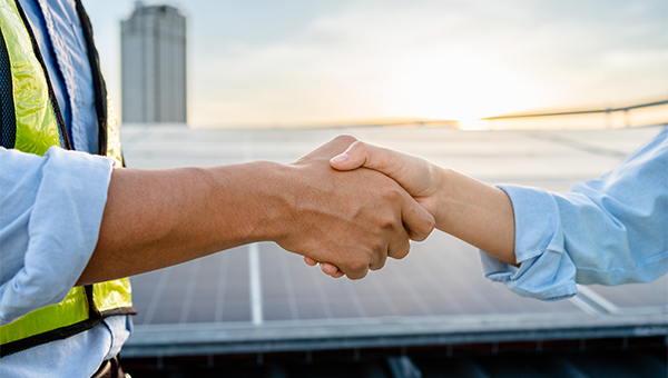 Two people shake hands in front of solar panels, suggesting a business agreement or partnership.